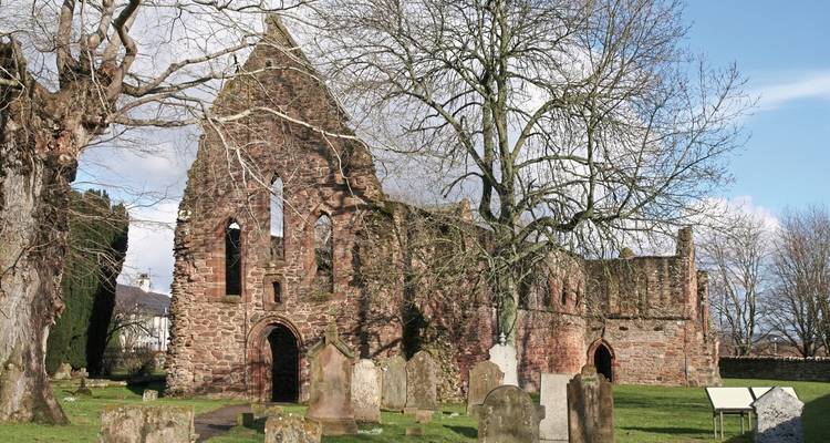 Ruins of an ancient stone structure surrounded by gravestones and trees.