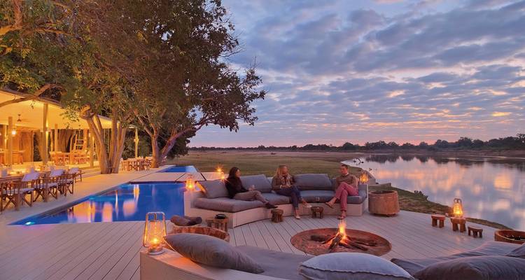 Espace de détente extérieur confortable au bord d'une piscine et d'une rivière au coucher du soleil.
