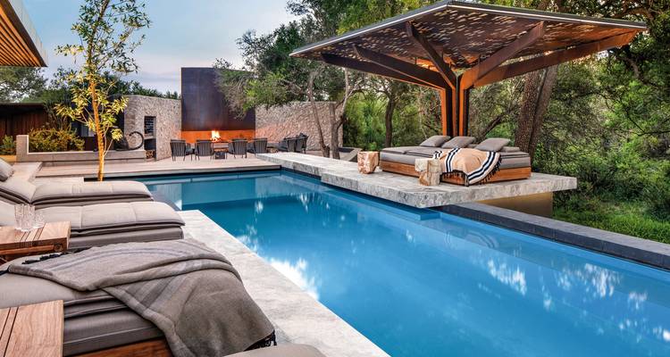 Hölzerne Poolterrasse mit Liegebetten und einem Kamin.