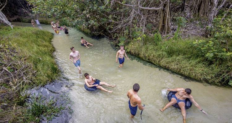 People enjoying a natural lazy river surrounded by greenery.