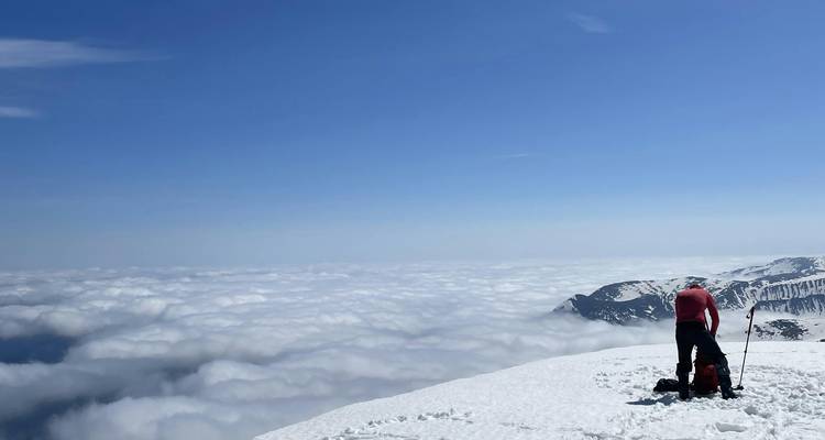 Lone hiker standing on a snow-covered peak overlooking a sea of clouds.