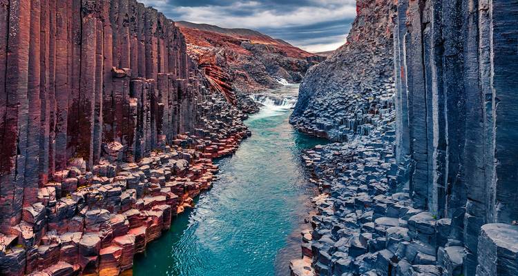 La rivière turquoise traverse des colonnes de basalte imposantes dans un canyon islandais accidenté.