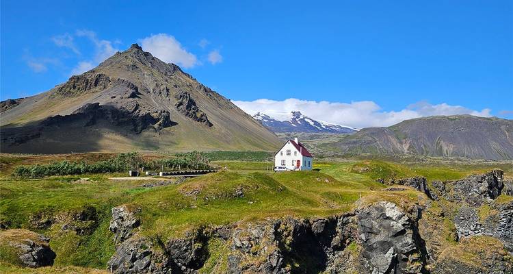 Una encantadora casita blanca en acantilados verdes y exuberantes bajo un pico volcánico accidentado en Snæfellsnes.
