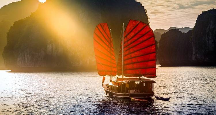 Dschunke mit roten Segeln in der Halong-Bucht bei Sonnenuntergang.