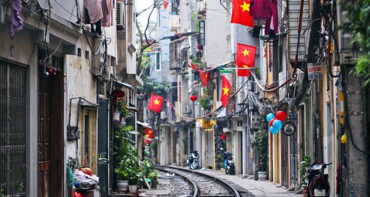 Straßenszene in Hanoi mit Bahngleisen und lokalen Flaggen.