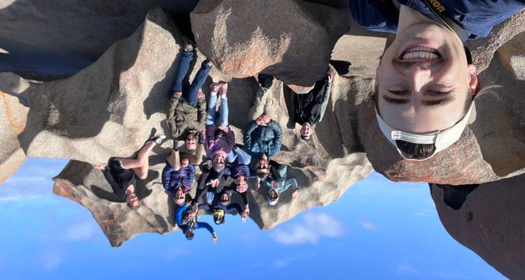 Selfie de un guía sonriente con un grupo sentado en las dramáticas rocas de granito con motas naranjas de Remarkable Rocks