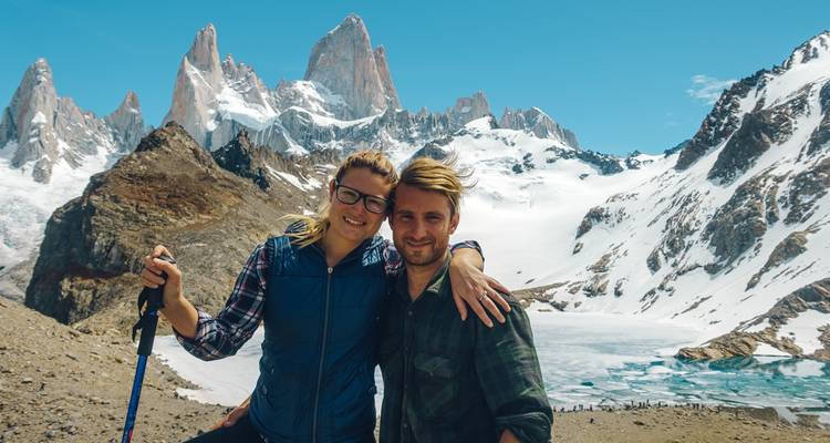 A couple posing in front of snowy mountains and a frozen lake.