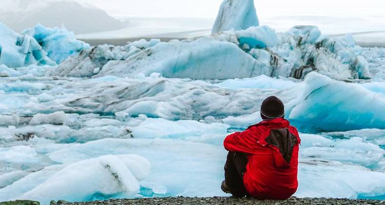 Persona con chaqueta roja sentada en el suelo mirando paisajes helados.