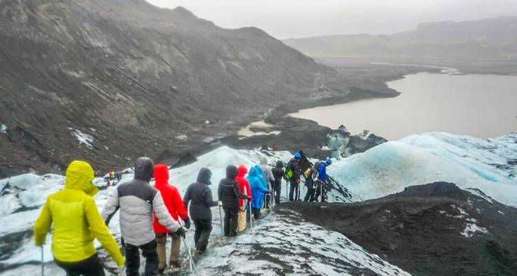 Grupo de personas haciendo senderismo en un glaciar en terreno accidentado.