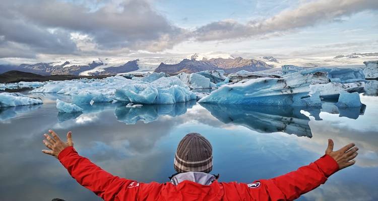 Personne les bras ouverts face à un lac glacé réfléchissant.