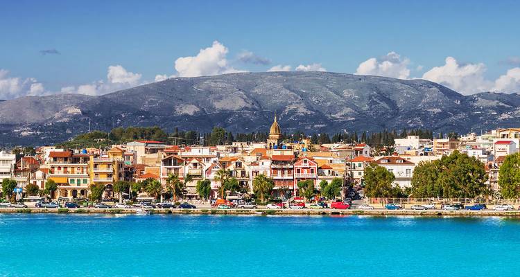 Helder stadje aan het water met bergen op de achtergrond en een turquoise baai op Zakynthos.