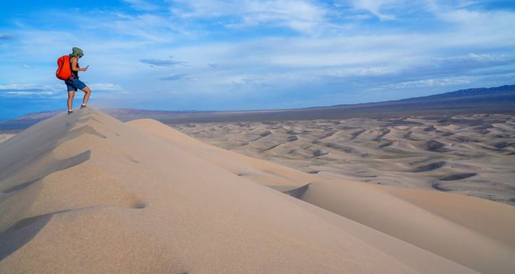 A person hiking on sand dunes under a blue sky.