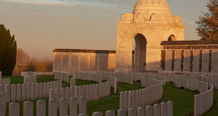 Cementerio de guerra sereno al amanecer con filas de lápidas blancas que conducen a un arco memorial con cúpula