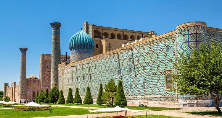 Madraza de cúpula azul con elaborados azulejos en una plaza soleada.