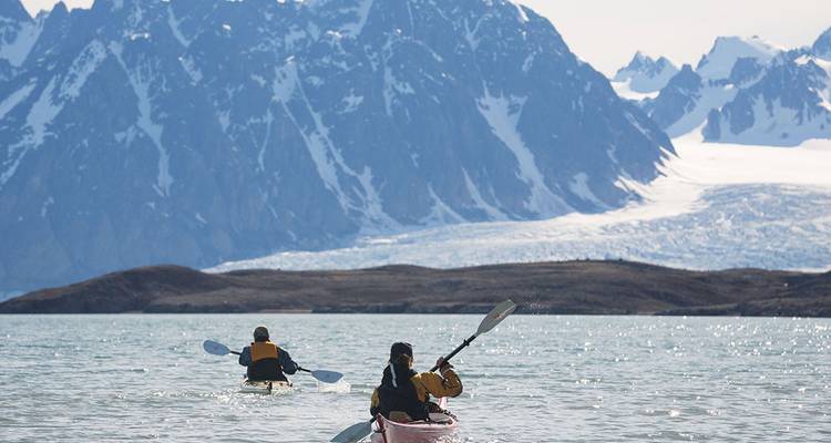 Deux kayakistes pagaient à travers des eaux d'un bleu glacé vers des pics déchiquetés couverts de glaciers sous un soleil éclatant.