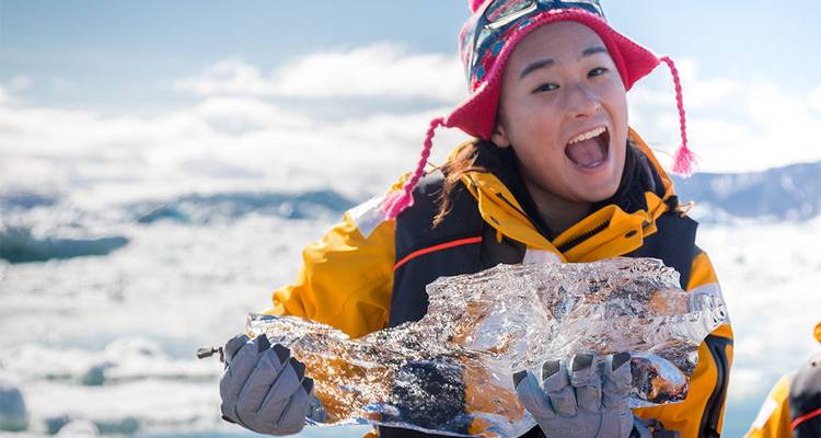 Voyageur souriant en parka jaune tient fièrement un morceau étincelant de glace glaciaire sur fond d'icebergs flottants.
