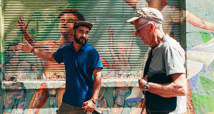 Guía local conversa junto a un mural de arte callejero colorido en un escaparate de chapa ondulada.