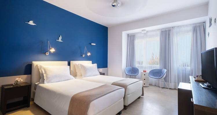 Chambre d'hôtel moderne et lumineuse avec deux lits jumeaux soigneusement préparés et un mur d'accent bleu.