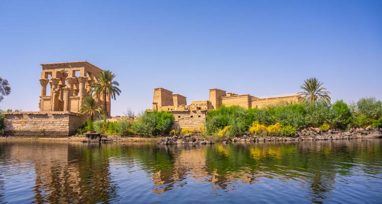 Temple de Philae vu depuis le Nil avec des reflets dans l'eau calme.