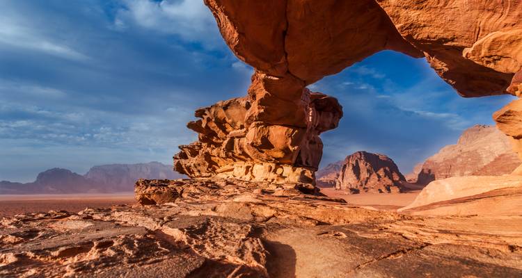 Formation d'arche spectaculaire en grès rouge dans le désert du Wadi Rum sous un ciel bleu.