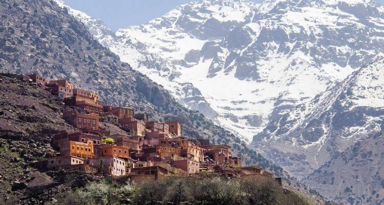 A village on a hillside with snowcapped mountains in the background.