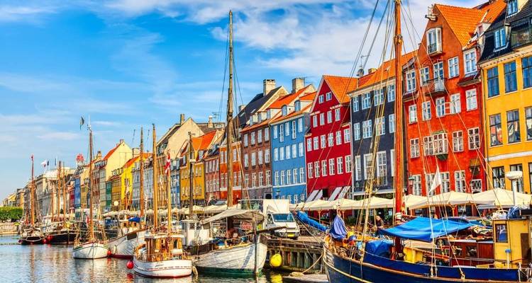Casas coloridas en el frente del agua y barcas de madera amarradas a lo largo del Nyhavn de Copenhague bajo un cielo azul brillante.