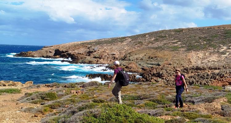 Les randonneurs traversent une végétation côtière rocheuse au-dessus des vagues bleu profond de la mer Égée sur l'île d'Andros.