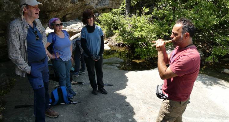Le guide joue de la flûte en bois tandis que les randonneurs se reposent dans une alcôve rocheuse ombragée sur Andros.