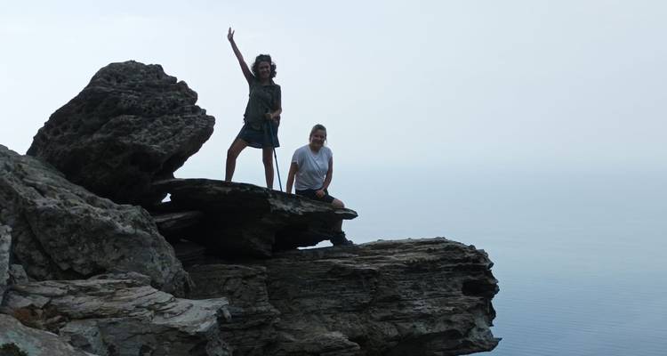 Deux randonneurs célèbrent au sommet d'une falaise côtière escarpée avec un horizon brumeux au-delà.