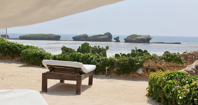 Vista de playa con un banco de cara al océano y formaciones rocosas en la distancia.