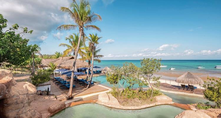 Resort tropical junto a la playa con piscinas y palmeras.