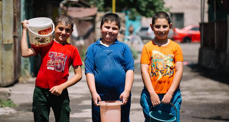 Trois garçons tenant des seaux et souriant à la caméra dans un cadre extérieur.