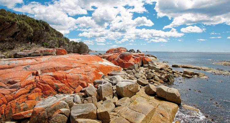 Rocks with orange hues by the sea under a blue sky.