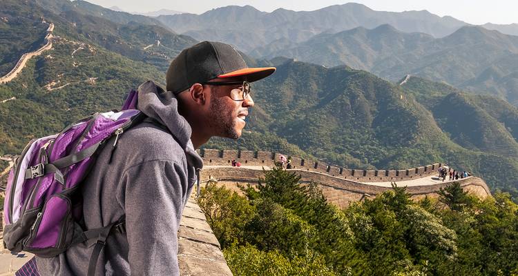 Un viajero contempla la Gran Muralla China serpenteando sobre montañas verdes.