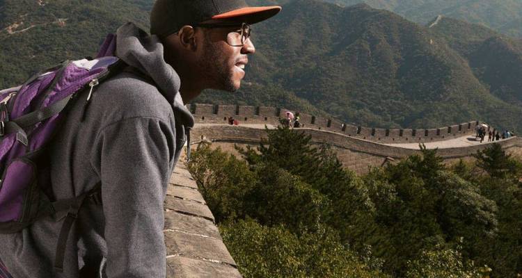Un voyageur s'appuie sur la Grande Muraille de Chine, admirant les montagnes boisées qui s'étendent au loin.