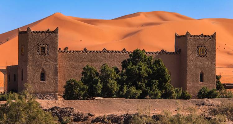 Traditionelles Gebäude mit Bäumen und Sanddünen.
