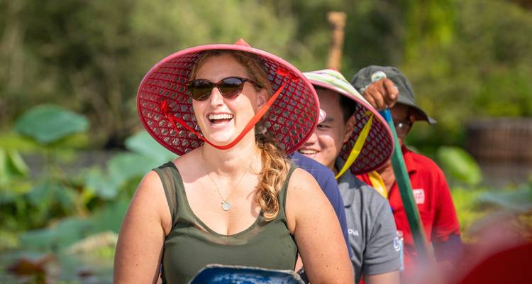 Touristes souriants portant des chapeaux traditionnels dans un bateau.