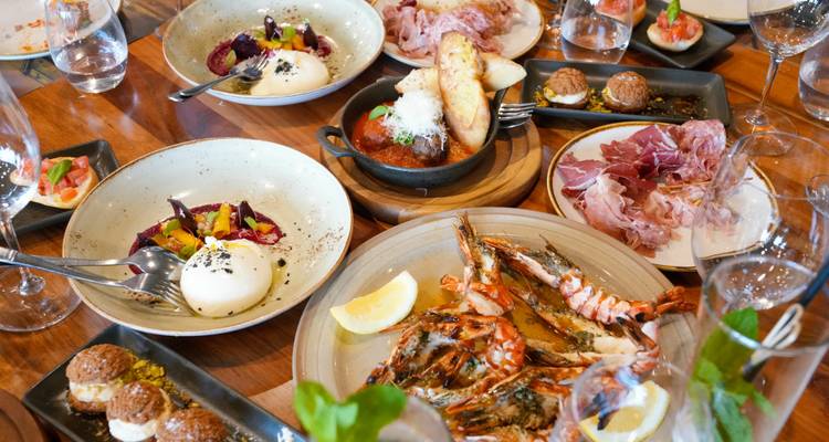 Variados platos ibéricos que incluyen mariscos, burrata, carnes curadas y tapas dispuestos en una mesa de madera.