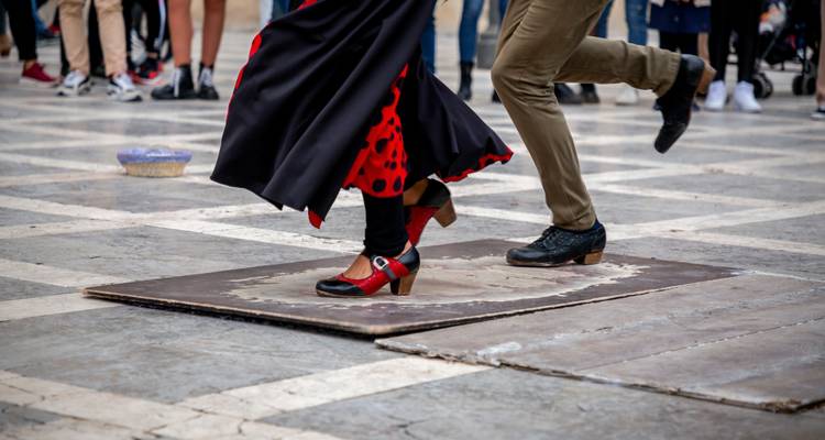 Primer plano de los pies de bailaores de flamenco en movimiento sobre una plataforma de madera en una plaza pública.