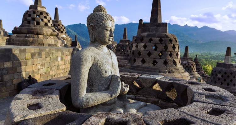 Buddha statue at Borobudur temple complex with distant mountain view.