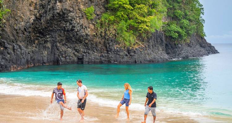 Four people playing in the waves on a beach with rocky cliffs.