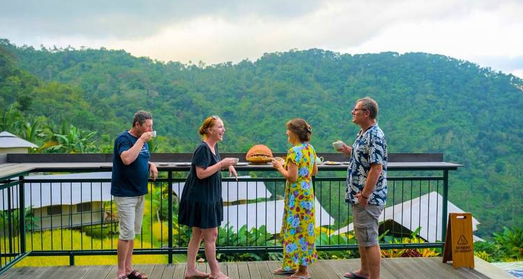 Four adults enjoy snacks and drinks on a terrace overlooking lush hills.