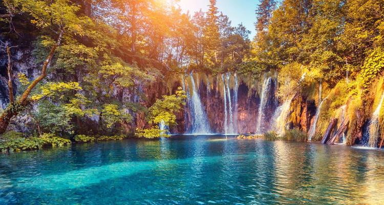 Beautiful lake with multiple cascading waterfalls surrounded by lush greenery.