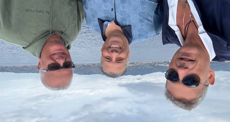 Drie mensen poseren op een boot met uitzicht op de bergen.