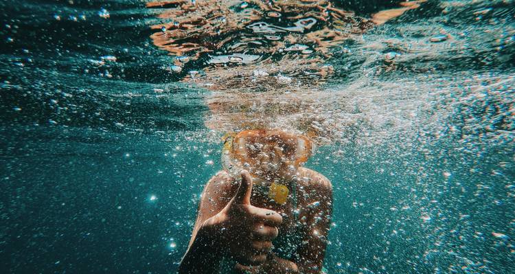 Persona haciendo snorkel bajo el agua haciendo un gesto de pulgar arriba.