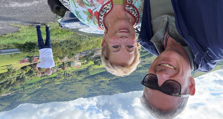 Un selfie de deux personnes avec une colline verdoyante pittoresque en arrière-plan.