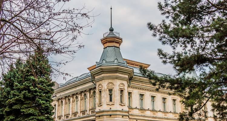Historic neoclassical building with spired roof framed by trees under cloudy sky.