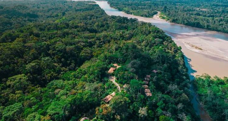 Luchtfoto van dicht Amazonisch regenwoud dat zich uitstrekt langs een kronkelende rivier met kleine lodge-open plekken