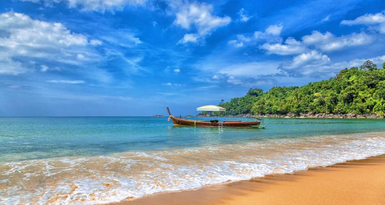 Longtailboot an einem tropischen Strand in Phuket mit ruhigem türkisfarbenem Wasser.