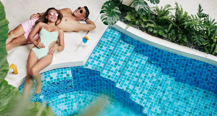 Stel ontspant bij een zwembad met drankjes.